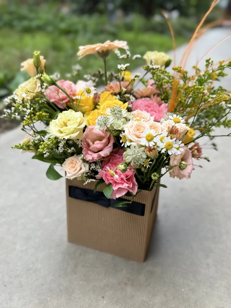 Arrangement floral Le Cubique, composé de fleurs frâiches dans les tons rose et jaune selon fleurs de saison