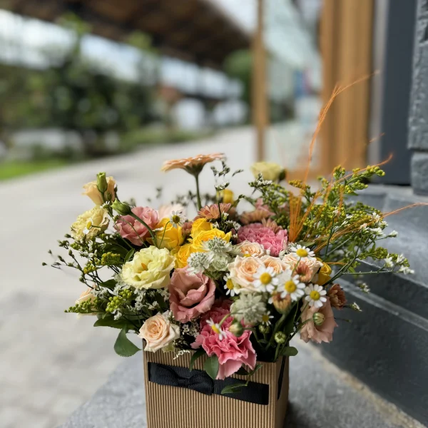 Arrangement floral Le Cubique, composé de fleurs frâiches dans les tons rose et jaune selon fleurs de saison