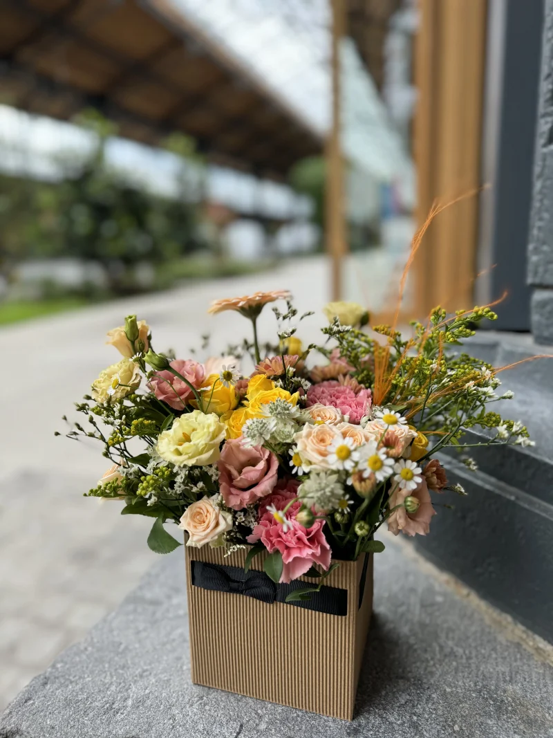 Arrangement floral Le Cubique, composé de fleurs frâiches dans les tons rose et jaune selon fleurs de saison